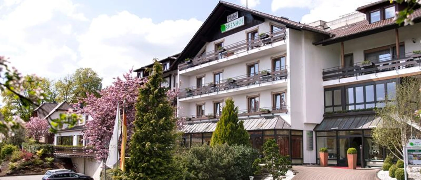 Hotel Birkenhof Rechteinhaber Ein Hotelgebäude "Birkenhof" mit Parkplatz, Bäumen und blühenden Sträuchern.