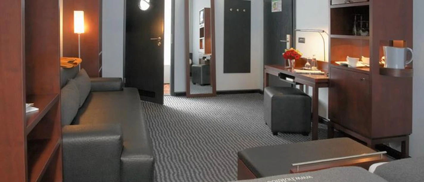 Hotel Concorde Rechteinhaber Ein Hotelzimmer mit grauem Sofa, Holzmöbeln und einem Fernseher.
