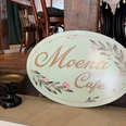 Café Moena Grünes Schild mit geschwungener Schrift "Moena Café"