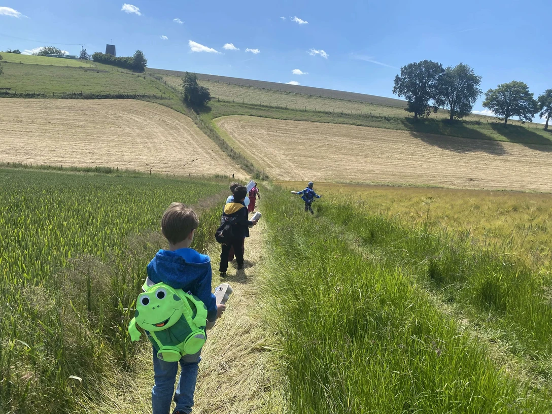 Kinderwanderung in Velbert Kinder wandern auf einem schmalen Pfad durch die Felder bei Velbert, jedes trägt einen Rucksack.