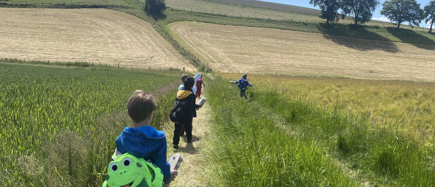Kinderwanderung in Velbert Kinder wandern auf einem schmalen Pfad durch die Felder bei Velbert, jedes trägt einen Rucksack.