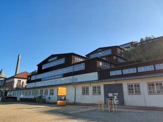 Erzaufbereitung am Weltkulturerbe Rammelsberg Im klaren Licht des Tages erhebt sich die historische Erzaufbereitungsanlage Rammelsberg mit markanten Backstein- und Fachwerkfassaden vor strahlend blauem Himmel.