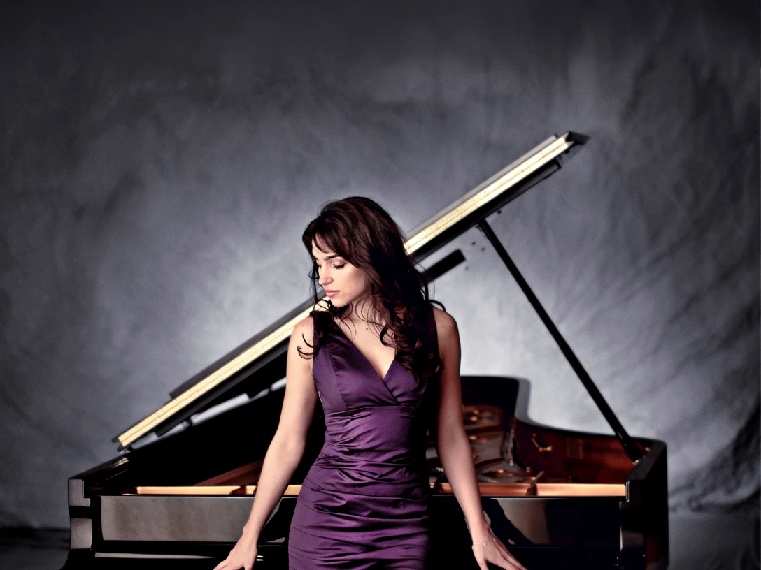 Olga Scheps Olga Scheps in elegantem, violettem Kleid sitzt verträumt an einem Flügel in stimmungsvollem Licht.