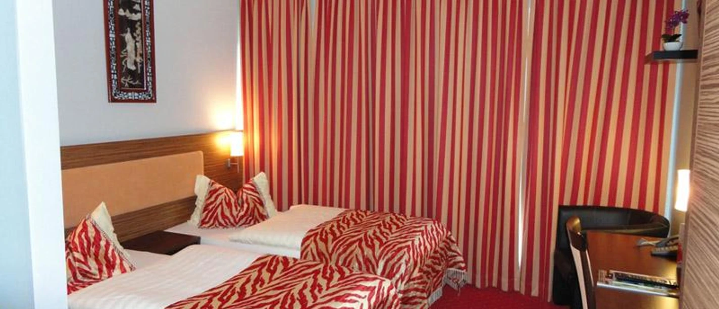 Grand Hotel Dream Frankfurt City Ein Hotelzimmer mit zwei Betten, roten Streifenvorhängen und rotem Teppich.