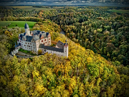 Lunzenau_Schloss Rochsburg_(c)Instagram _lng_photography__CC BY-SA (1).JPEG Das Foto zeigt einen Luftaufnahme von Schloss Rochsburg. Das Schloss ist umgeben von einem golden schimmernden Herbtwald.The photo shows an aerial view of Rochsburg Castle. The castle is surrounded by a shimmering golden autumn forest.Na fotografii je letecký pohled na hrad Rochsburg. Hrad je obklopen třpytivým zlatým podzimním lesem.Zdjęcie przedstawia widok zamku Rochsburg z lotu ptaka. Zamek otoczony jest mieniącym się złotą jesienią lasem.De foto toont een luchtfoto van kasteel Rochsburg. Het kasteel wordt omringd door een glinsterend gouden herfstbos.La foto mostra una veduta aerea del castello di Rochsburg. Il castello è circondato da una scintillante foresta autunnale dorata.