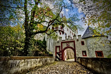 Lunzenau_Schloss Rochsburg_(c)Instagram _lng_photography__CC BY-SA (2).JPEG You can see the entrance to the grounds of Rochsburg Castle. It is a pretty archway. The autumnal trees are dropping their leaves, which gather in front of the gate.