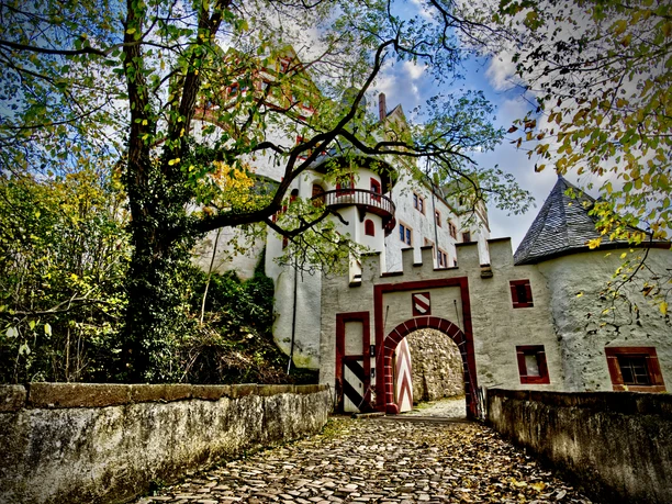 Lunzenau_Schloss Rochsburg_(c)Instagram _lng_photography__CC BY-SA (2).JPEG You can see the entrance to the grounds of Rochsburg Castle. It is a pretty archway. The autumnal trees are dropping their leaves, which gather in front of the gate.