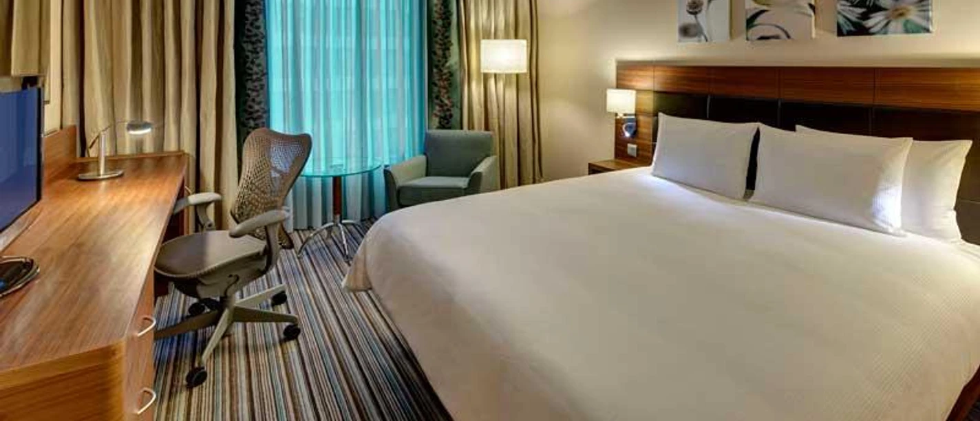 Hilton Garden Inn Frankfurt Airport Ein modernes Hotelzimmer mit großem Bett, Schreibtisch und gestreiftem Teppich.