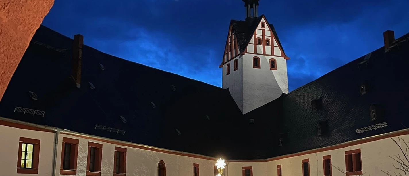 Zu sehen ist der stimmungsvoll geschmückte Hof von Schloss Rochsburg. Die Lampen am Weihnachtsbaum leuchten und es findet gerade der Adventsmarkt statt.
