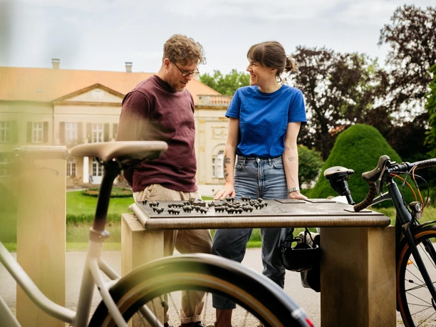 Schloss Harkotten Een man en een vrouw kijken naar een miniatuurmodel van een park omringd door fietsen.