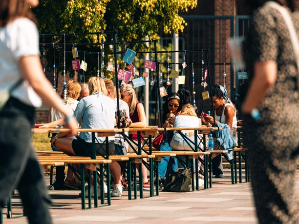 Even Flow Festival 2025 People sit at outdoor beer tables surrounded by green trees at a lively event.