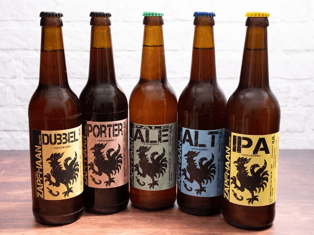 Alle fünf Biersorten von Zapfhaan aus Haan Fünf Zapfhaan Biersortenflaschen in Haan vor weißem Hintergrund, jede mit einem markanten Etikett.