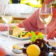 Zu Tisch im Zum Vater Rhein Hotel & Restaurant in Monheim am Rhein In einem eleganten Restaurant wird Weißwein in hohe Gläser geschenkt, während ein delikates Essen serviert wird.