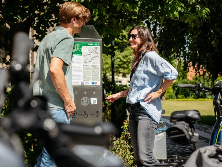 Hörstation an der Friedensroute Zwei Personen studieren eine Informationstafel für Radtouren. Im Vordergrund Fahrräder.Two people studying an information board for cycle tours. Bicycles in the foreground.To personer studerer en informationstavle for cykelture. Cykler i forgrunden.Twee mensen bestuderen een informatiebord voor fietstochten. Fietsen op de voorgrond.