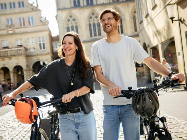 Prinzipalmarkt in Münster Een man en een vrouw duwen hun fietsen door een historische steeg bij zonnig weer.