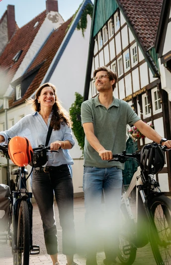 Unterwegs in der Altstadt von Osnabrück Zwei Personen laufen mit Fahrrädern durch eine gepflasterte Straße mit Fachwerkhäusern.