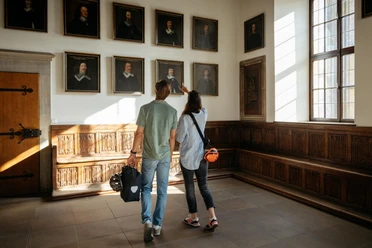 Der Friedenssaal im Osnabrücker Rathaus Two visitors look at paintings in a historic room with wood paneling and large windows.