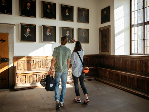 Der Friedenssaal im Osnabrücker Rathaus Twee bezoekers bekijken schilderijen in een historische kamer met houten lambrisering en grote ramen.