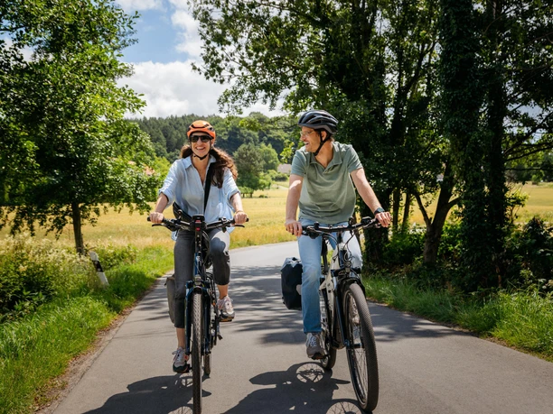 Unterwegs auf der Friedensroute im Osnabrücker Land Two cyclists on a rural road, surrounded by green trees and fields.
