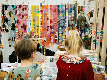 Der Super Weihnachtsmarkt Kinder betrachten bunte Mobile an einem Weihnachtsmarktstand mit farbenfrohem Hintergrund.Children look at colorful mobiles at a Christmas market stand with a colorful background.
