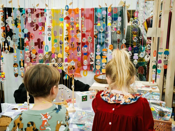 Children look at colorful mobiles at a Christmas market stand with a colorful background.