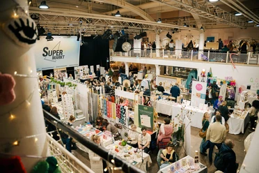Belebter Hallenmarkt mit Ständen für Kunst, Design und Handwerk auf zwei Ebenen