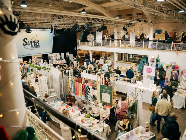 Busy indoor market with stalls and visitors browsing handmade goods on two levels
