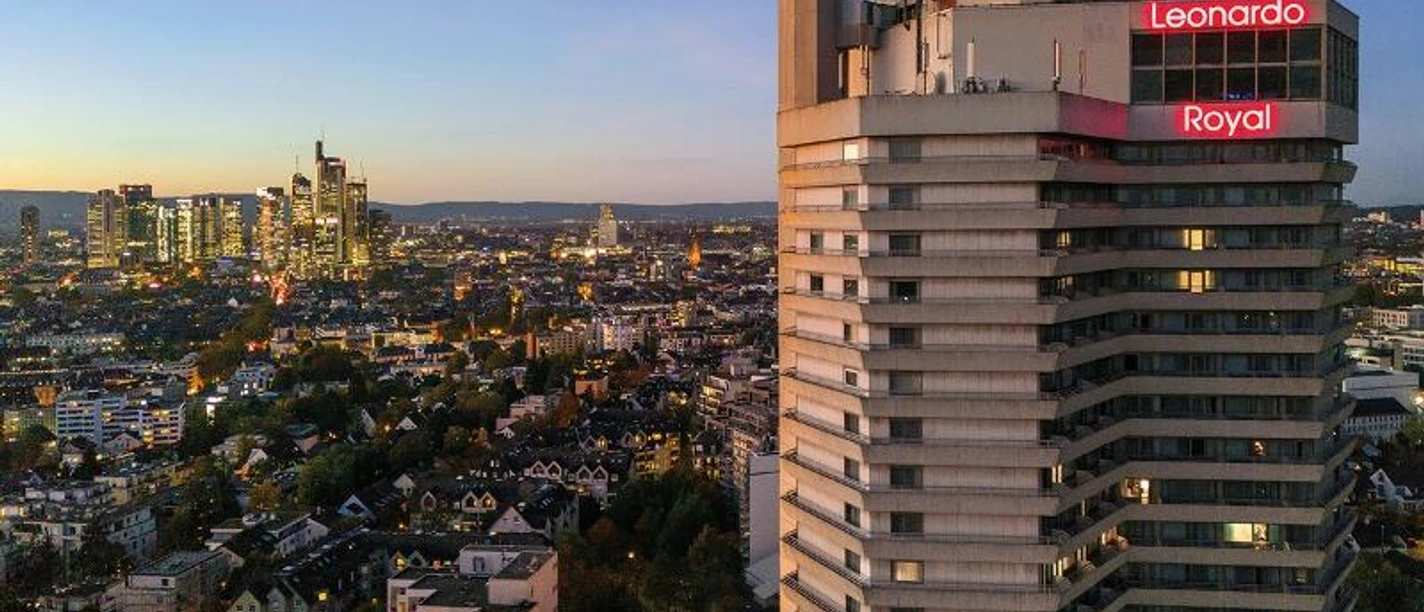 Leonardo Royal Frankfurt Ein hohes Hotelgebäude "Leonardo Royal" mit beleuchtetem Logo und Stadtblick bei Nacht.