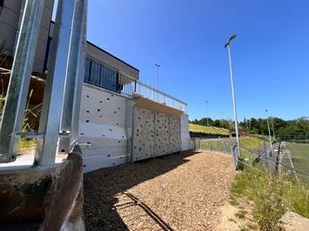 Kletterwand im Niedrigseilgarten in Heiligenhaus Kletterwand im Niedrigseilgarten Heiligenhaus, umgeben von Geländern und hellem Kiesweg.