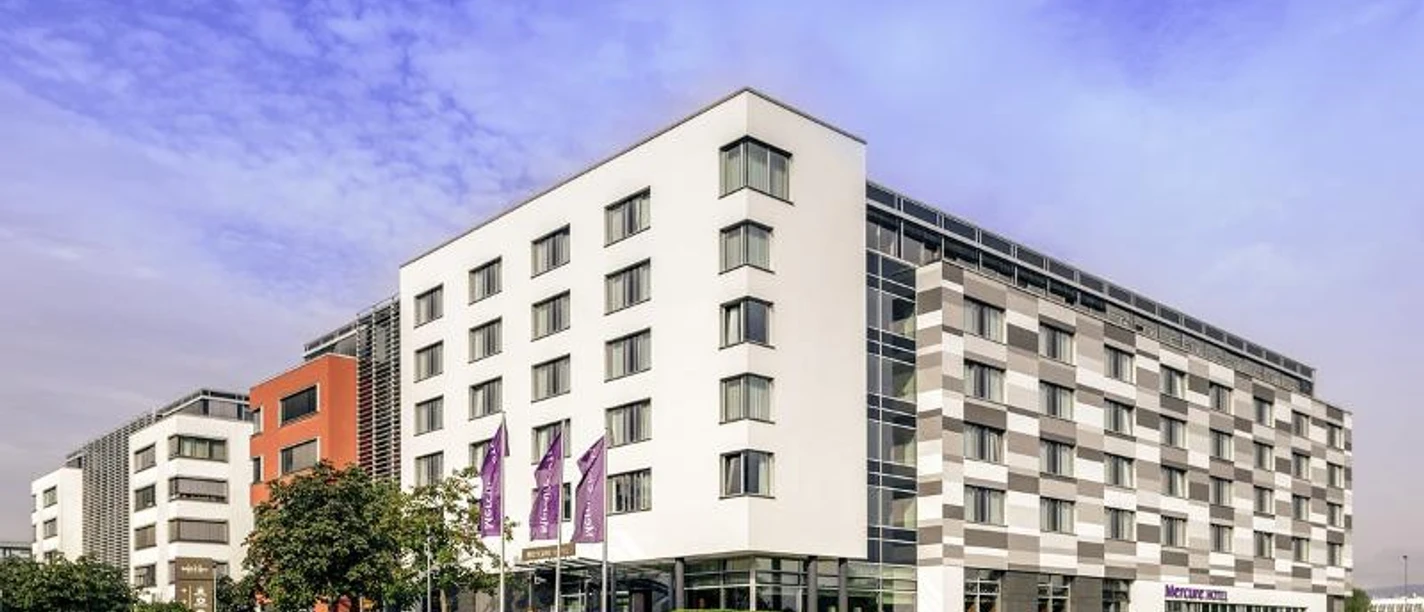 Mercure Hotel Frankfurt Eschborn Helfmann Park Ein modernes Mercure Hotelgebäude mit weißen, grauen und orangefarbenen Fassaden.