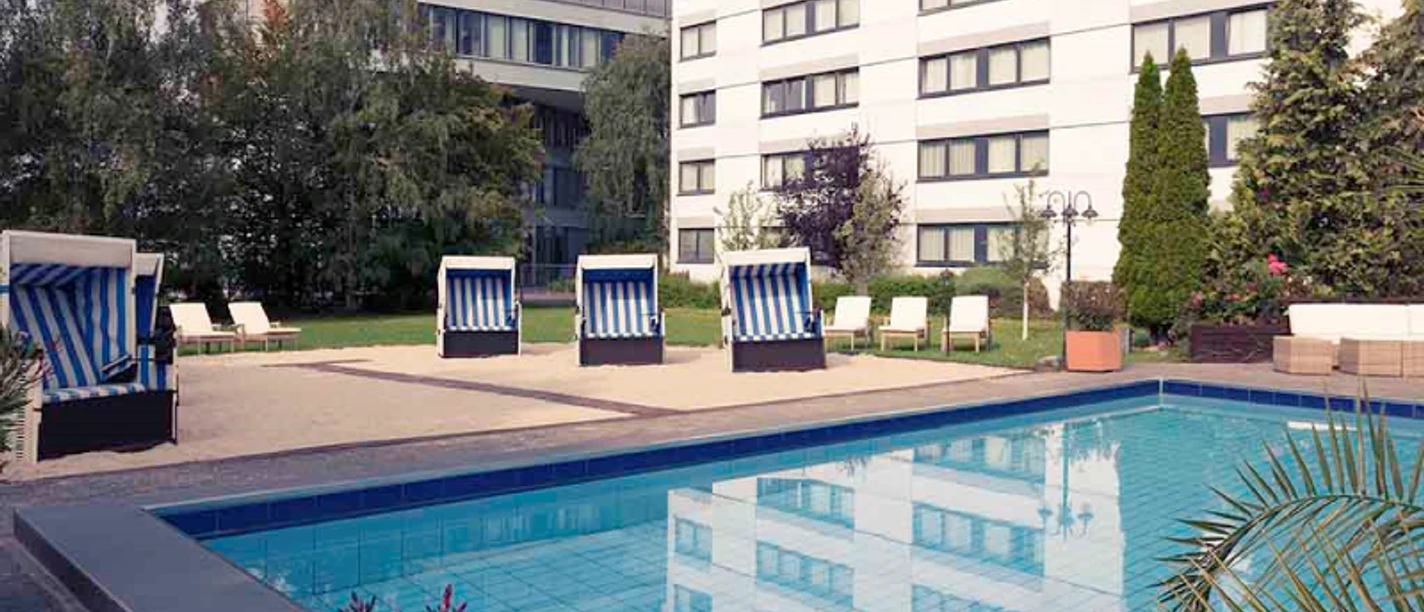 Mercure Hotel Frankfurt Eschborn Ost Ein Außenbereich mit Pool, Strandkörben und modernen Gebäuden.