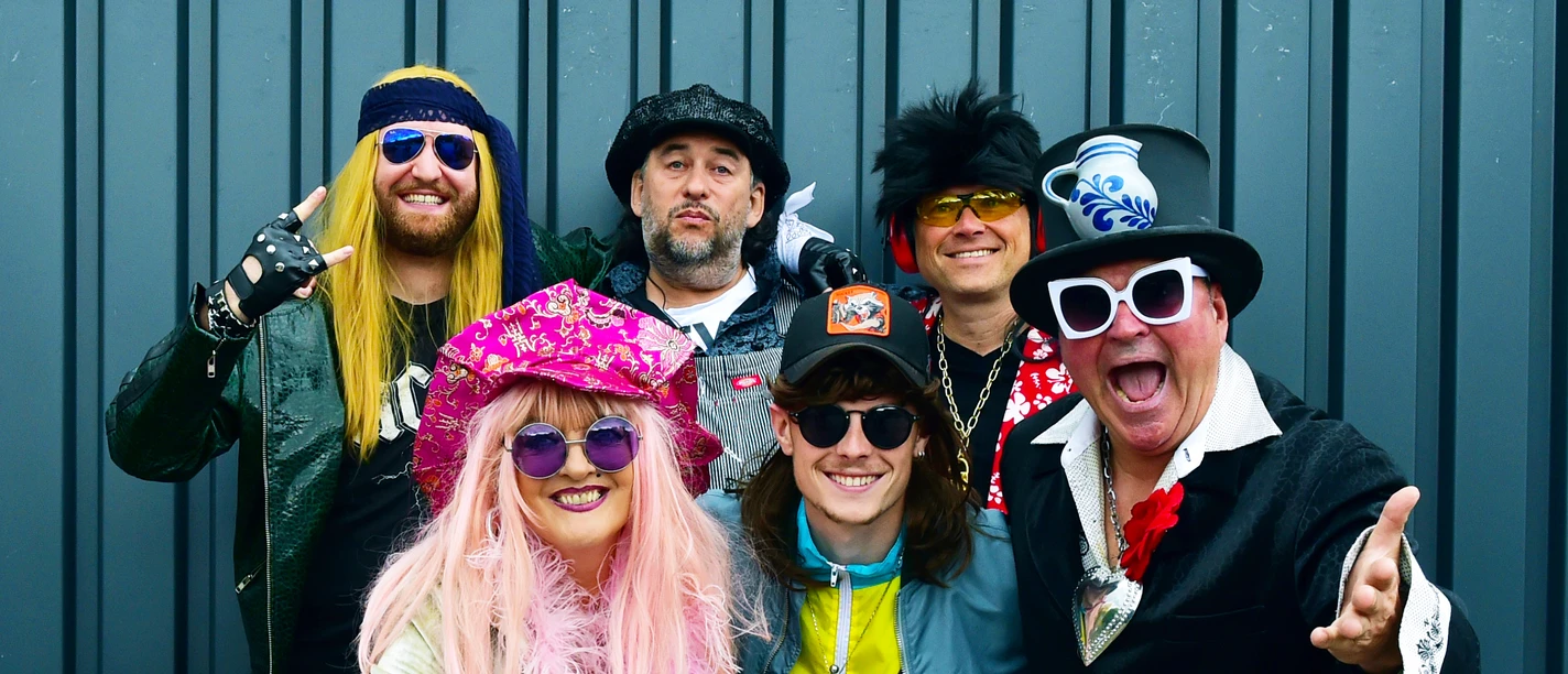 Roy Hammer & die Pralinées - Band Photo Group in colourful costumes in front of grey wall