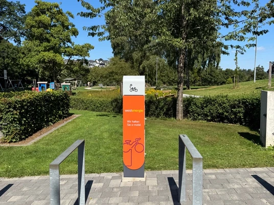Eine orangefarbene Akku-Ladestation für E-Bikes im Kurpark.