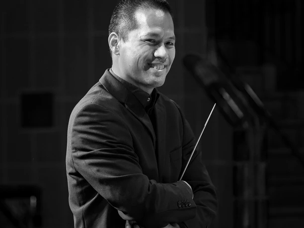 Timor Oliver Chadik Ein professionelles Schwarzweiß-Portrait zeigt einen lächelnden männlichen Dirigenten im Anzug.