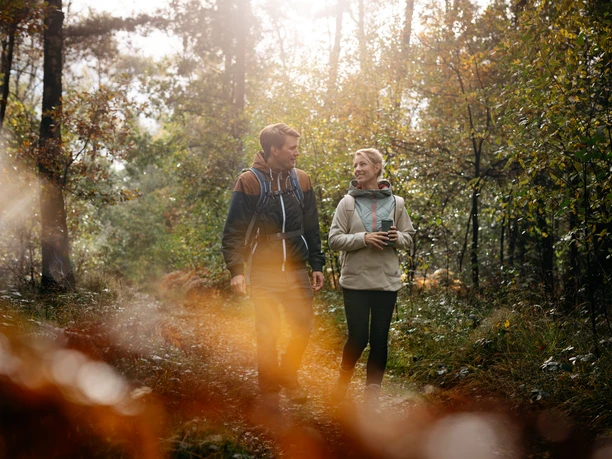 Twee mensen wandelen in een zonovergoten bos in herfstsfeer.