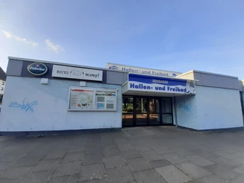 Infotafel beim Startpunkt von den VitalWege auf dem Parkplatz am Hallen- und Freibad Eingangsbereich des Hallen- und Freibads Einbeck mit blauer Beschilderung und Infotafel an der Wand