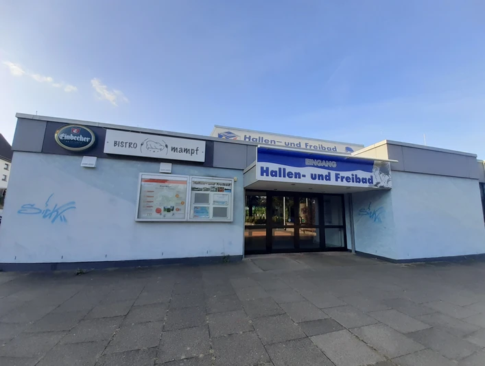 Infotafel beim Startpunkt von den VitalWege auf dem Parkplatz am Hallen- und Freibad Eingangsbereich des Hallen- und Freibads Einbeck mit blauer Beschilderung und Infotafel an der Wand