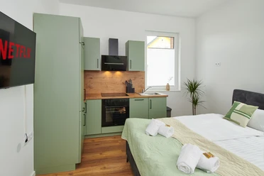 Wohn-/Schlafbereich mit Küchenzeile Wohn-/Schlafbereich mit grüner Küchenzeile, Doppelbett, TV, Fenster mit Tageslicht und Handtüchern.