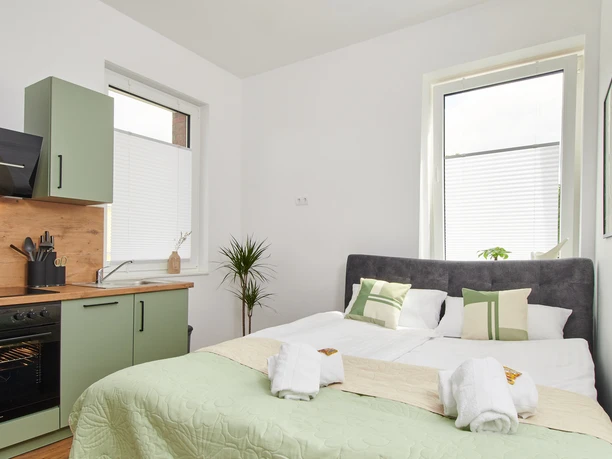 Schlafbereich Heller Raum mit Doppelbett, grüner Küche und großen Fenstern. Elegante Einrichtung und moderne Geräte.