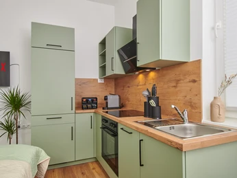 Küchenzeile Moderne Küche mit grünen Schränken, Holzarbeitsplatte, Edelstahlspüle und integrierten Elektrogeräten.