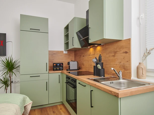 Küchenzeile Moderne Küche mit grünen Schränken, Holzarbeitsplatte, Edelstahlspüle und integrierten Elektrogeräten.