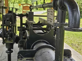 Eine historische Metallpumpe steht in grüner Natur nahe dem Feuerteich in Pömbsen.