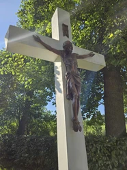 Kreuz nahe des Heiligenteiches in Pömbsen Kruzifix aus Holz mit Sonnenstrahlen, umgeben von grünem Laub.