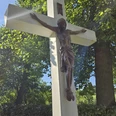 Kreuz nahe des Heiligenteiches in Pömbsen Kruzifix aus Holz mit Sonnenstrahlen, umgeben von grünem Laub.