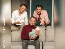 Drei Männer in gemütlicher Raumumgebung blicken lächelnd in die Kamera, einer hält ein Baby.