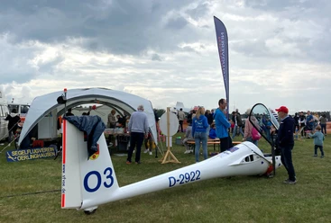 Menschen versammeln sich auf einer Wiese, um ein weißes Segelflugzeug mit türkisfarbenem Himmel.