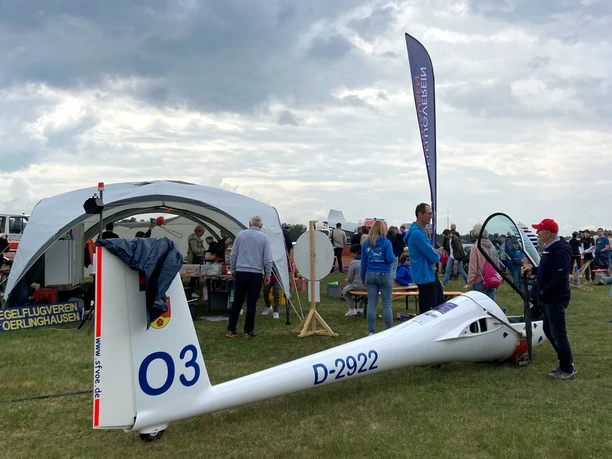 Menschen versammeln sich auf einer Wiese, um ein weißes Segelflugzeug mit türkisfarbenem Himmel.