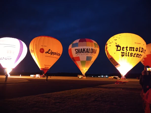 Heißluftballons erhellen in verschiedenen Farben das dunkle Abendhimmel bei einem Festival.