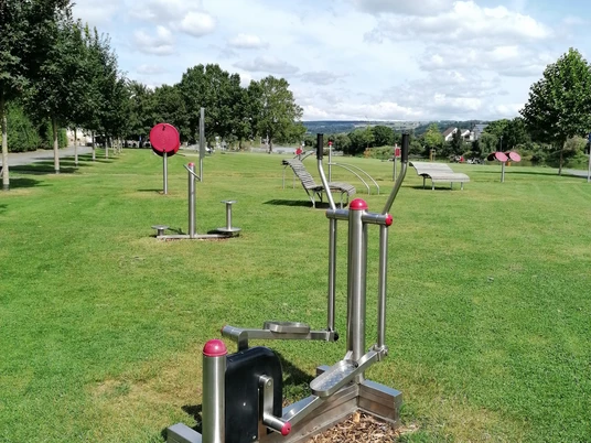 Ein Ganzkörpertrainer auf der Wiese, im Hintergrund weitere Fitnessgeräte des Beverunger Bewegungsparcours.
