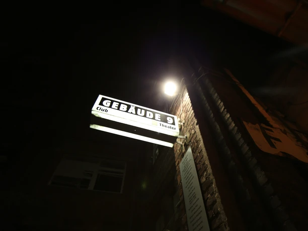 Gebäude 9 Building 9 is illuminated by a striking sign at night, with graffiti on the brick façade.